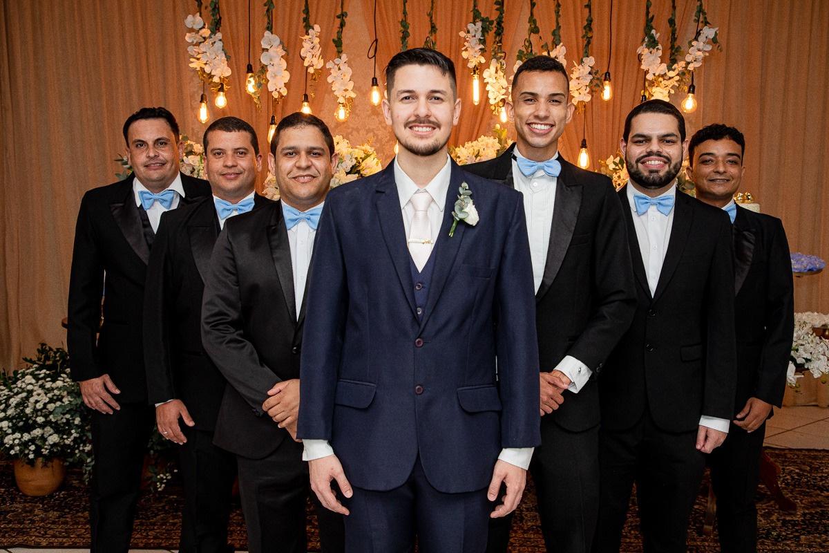 Imagem de padrinhos de casamento ao lado do noivo, todos usando ternos pretos elegantes, com expressões de felicidade e confraternização.